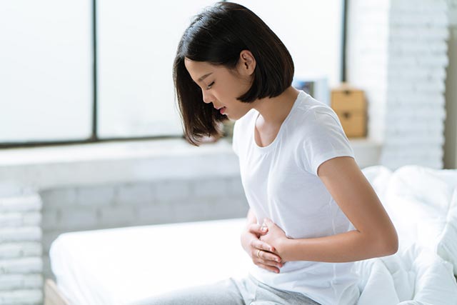 A young lady holding on to her tummy while sitting on the couch