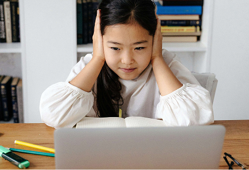 Child holding head while looking at a laptop, appearing stressed during study.
