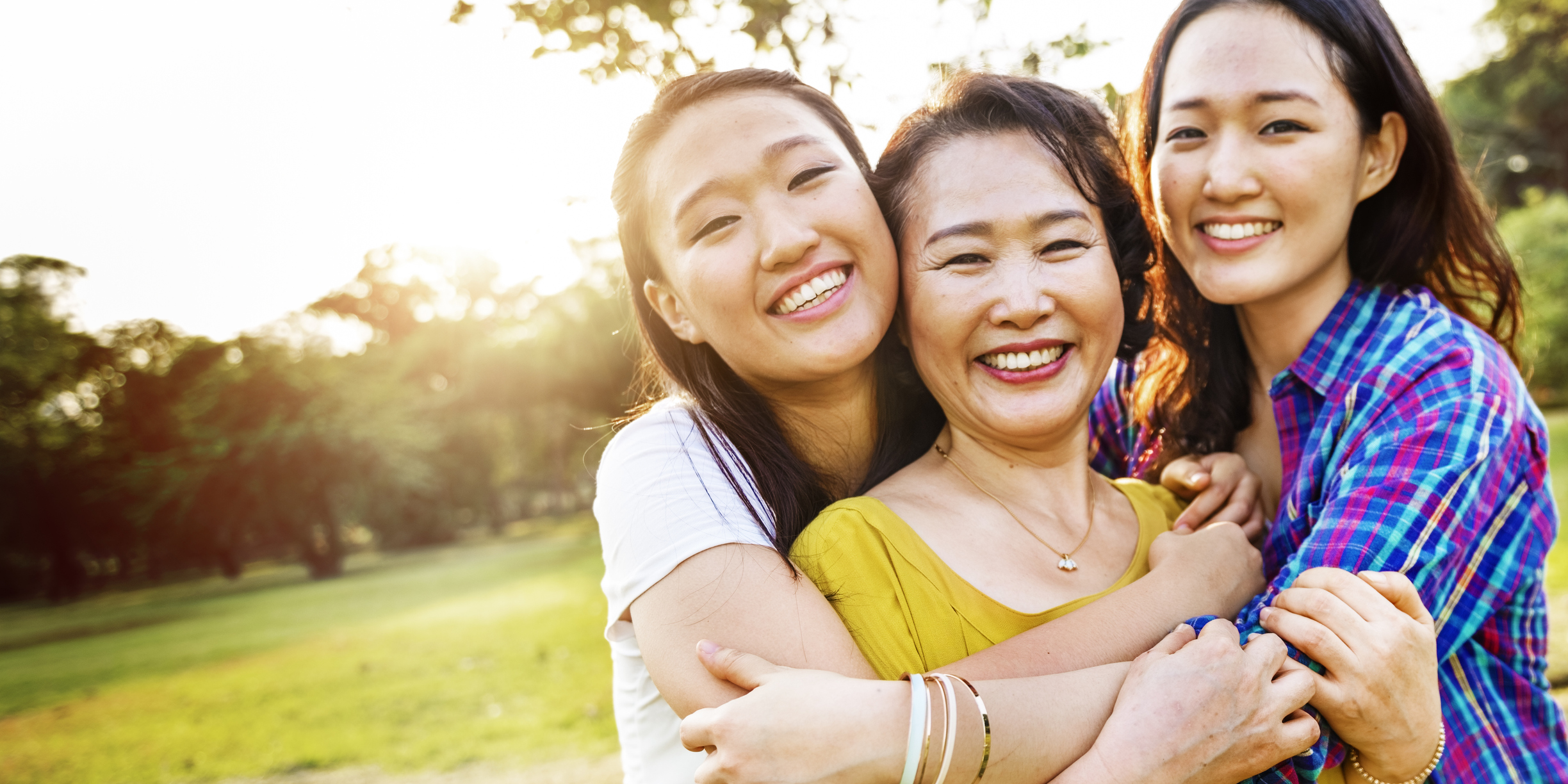 Mother with two young daughters kissing her cheek at a park